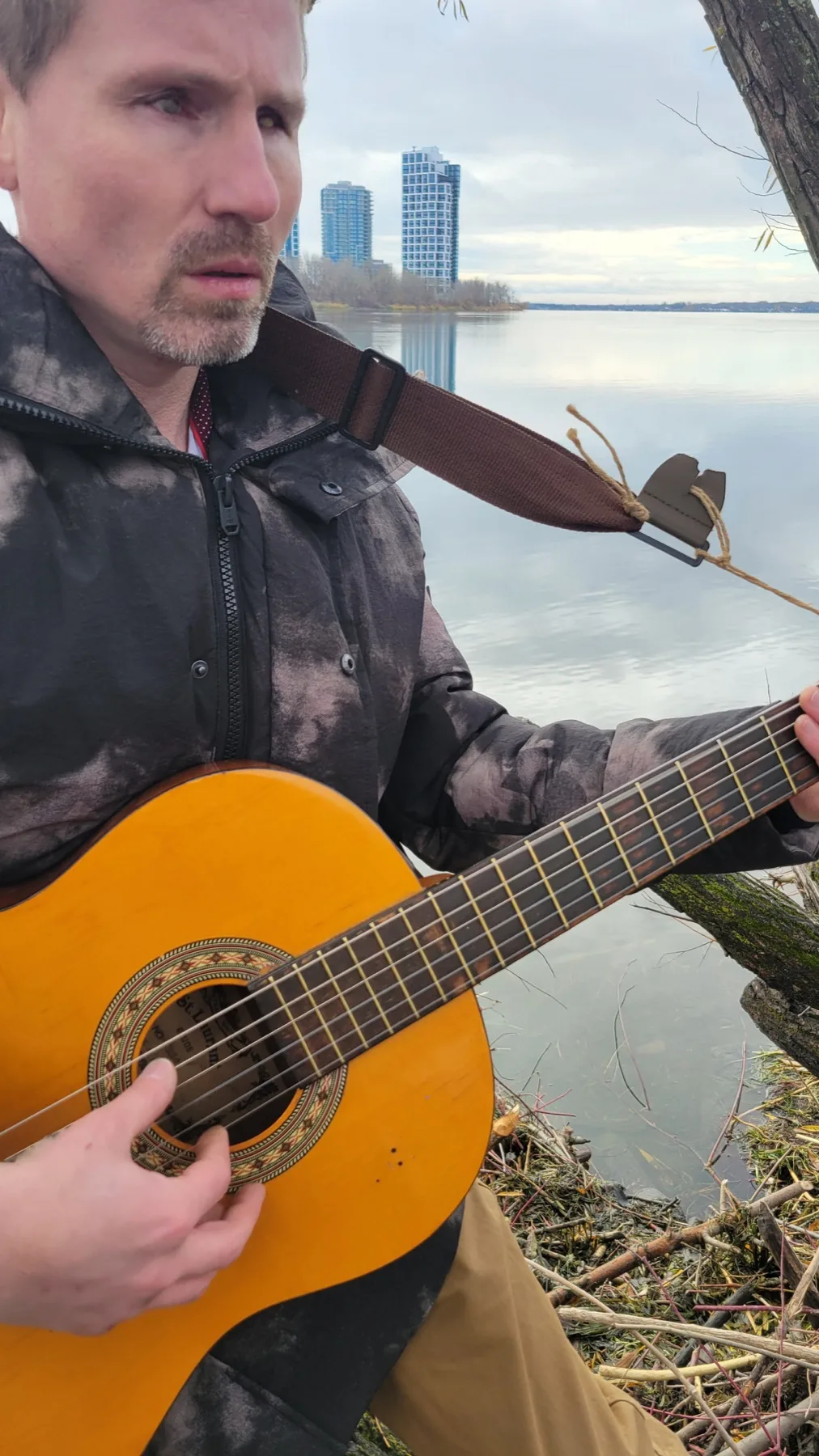 Devin playing an acoustic guitar beside the water in Montreal.